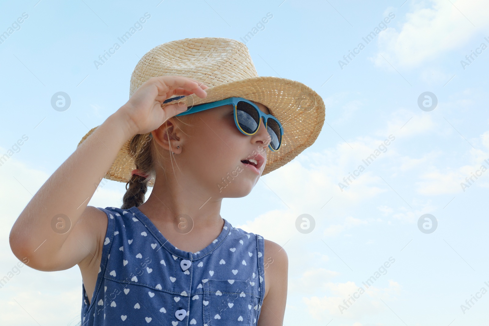 Photo of Little girl wearing sunglasses and hat at beach on sunny day