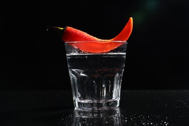 Photo of Red hot chili pepper and vodka in glass on black table