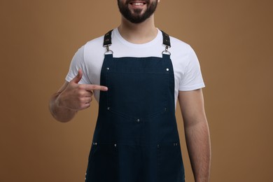 Photo of Smiling man pointing at kitchen apron on brown background, closeup. Mockup for design