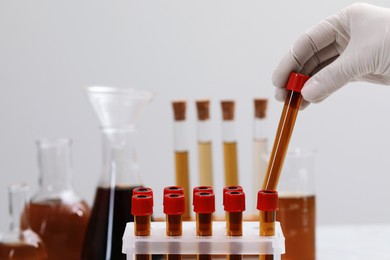 Photo of Scientist taking test tube with brown liquid from stand against light background, closeup