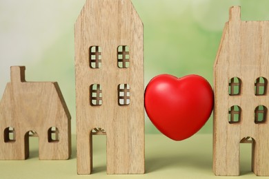 Photo of Long-distance relationship concept. Decorative heart between two wooden house models on light green background, closeup