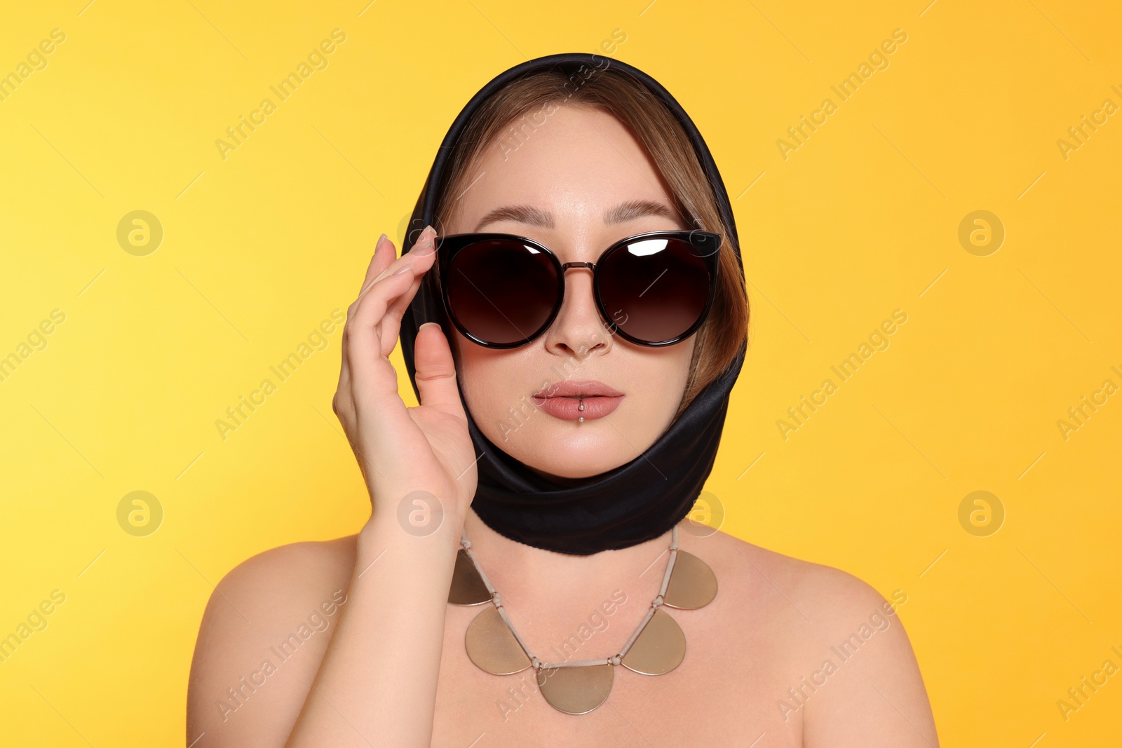 Photo of Young woman with lip piercing and sunglasses on yellow background