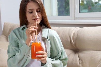 Photo of Beautiful young woman drinking juice from glass bottle on sofa at home