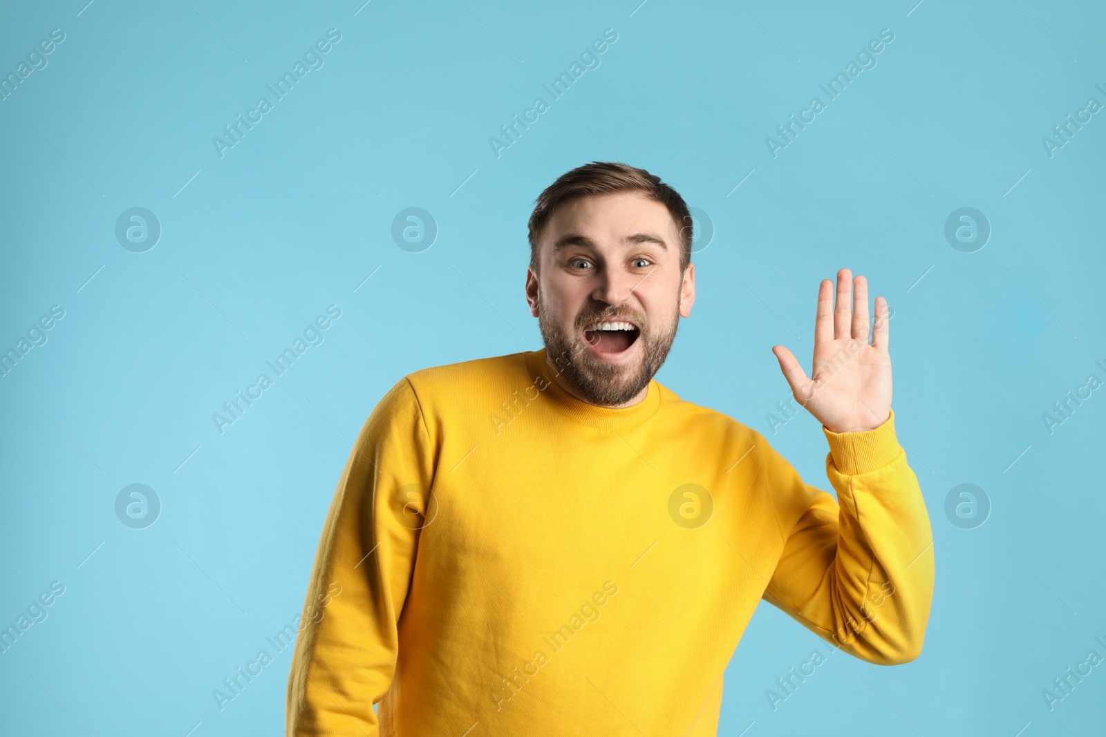 Photo of Happy young man waving to say hello on light blue background