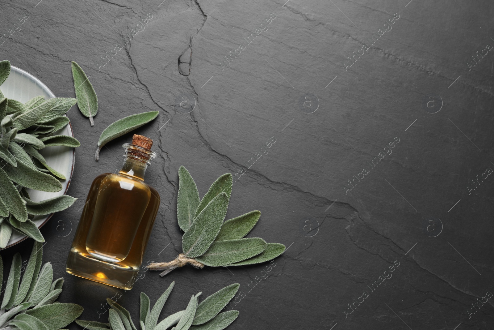 Photo of Bottle of essential sage oil and leaves on black table, flat lay. Space for text