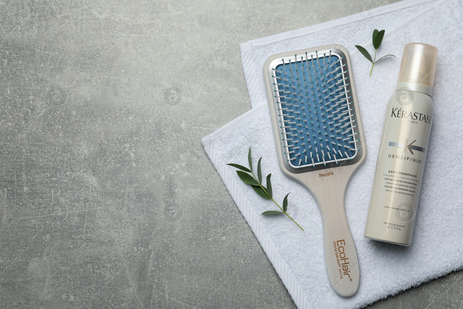 Photo of MYKOLAIV, UKRAINE - SEPTEMBER 07, 2021: Kerastase hair mousse, brush and towel on grey table, flat lay. Space for text