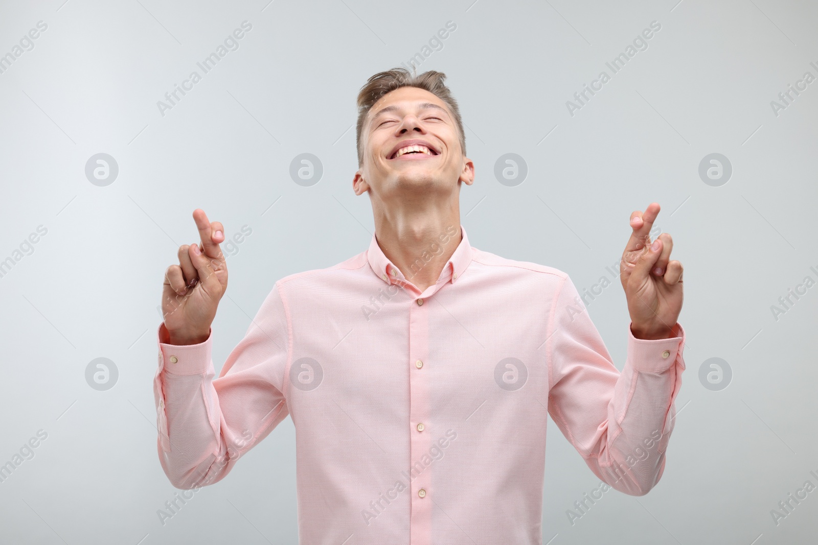 Photo of Happy young man crossing his fingers on light grey background