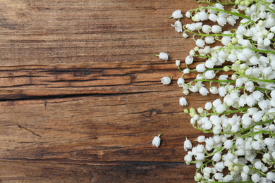 Beautiful lily of the valley flowers on wooden table, flat lay. Space for text