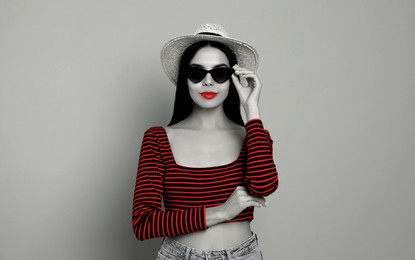 Attractive woman in stylish sunglasses on light grey background. Black and white photo with red accent