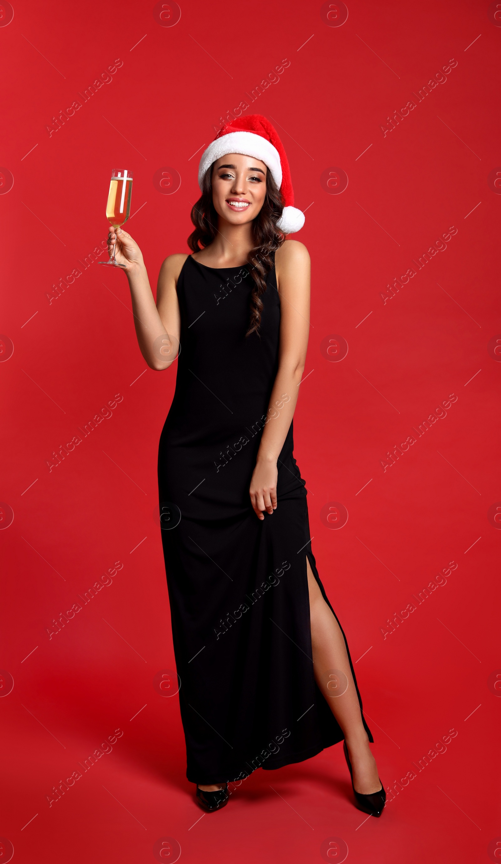 Photo of Beautiful woman in Santa hat holding glass of champagne on red background. Christmas party