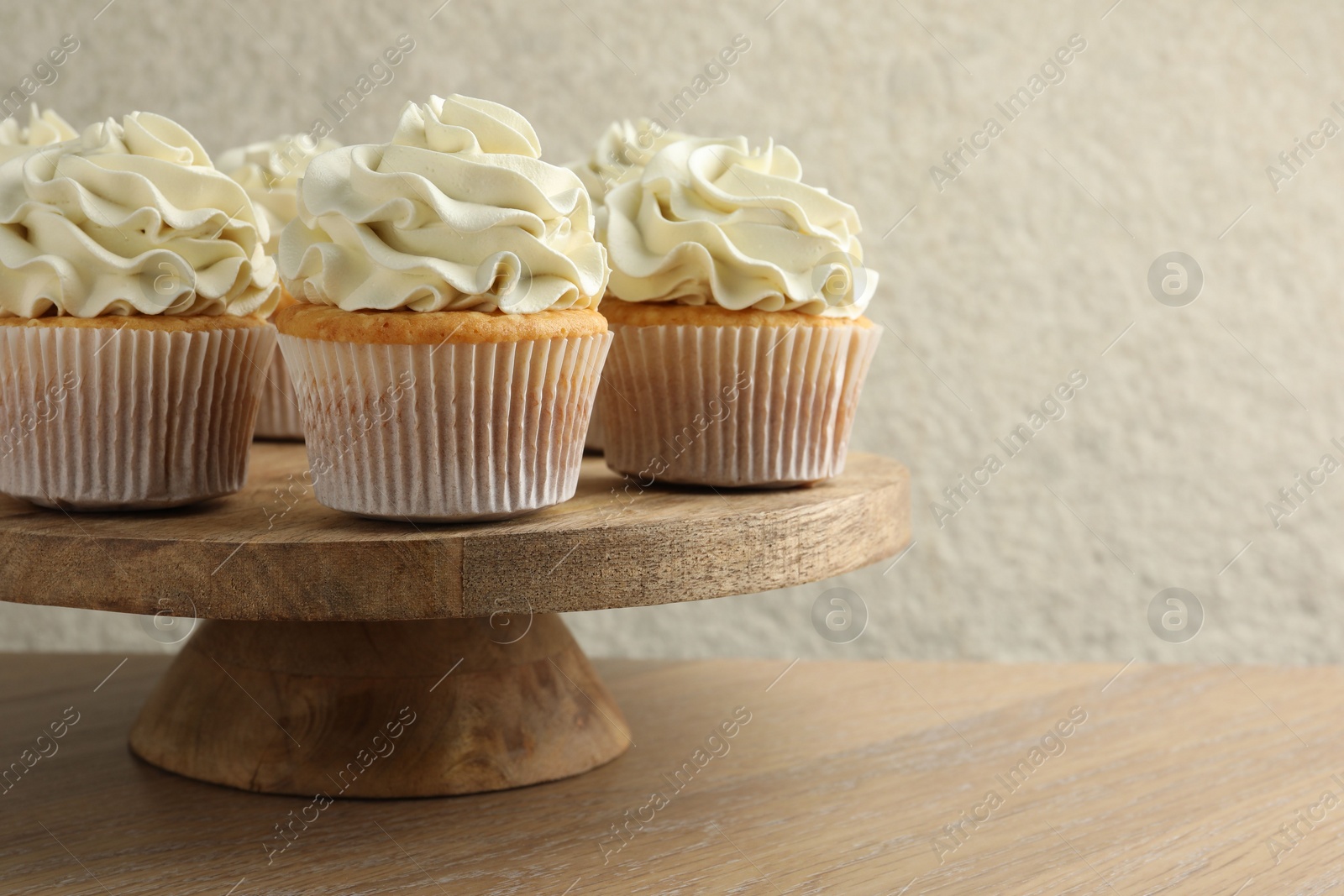 Photo of Tasty vanilla cupcakes with cream on wooden table, space for text