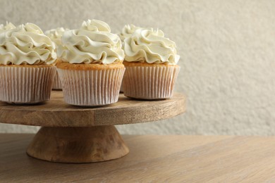 Tasty vanilla cupcakes with cream on wooden table, space for text