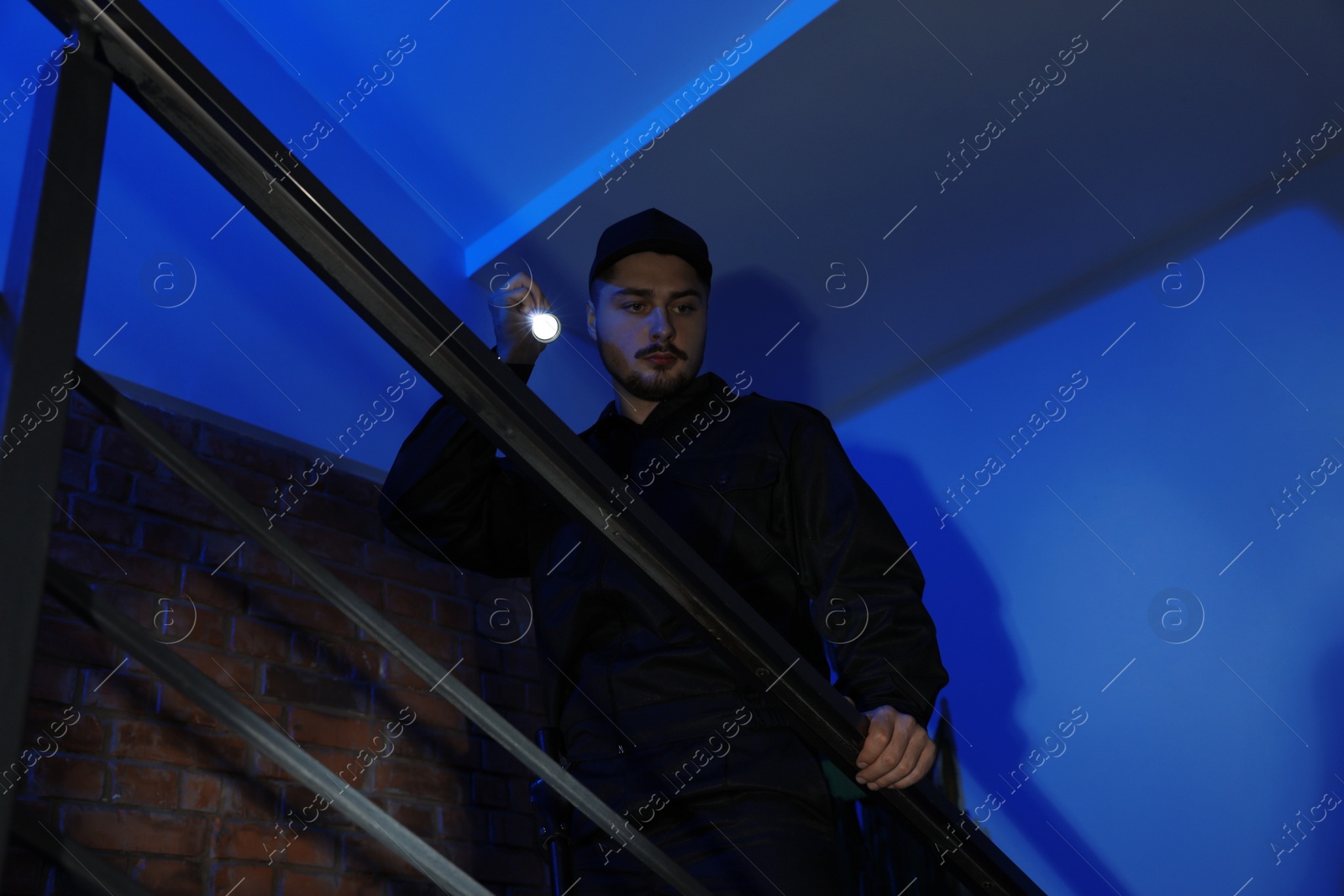 Photo of Male security guard with flashlight on stairs in darkness