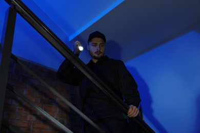 Photo of Male security guard with flashlight on stairs in darkness