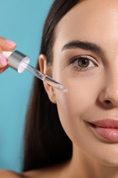 Photo of Beautiful young woman applying serum onto her face on light blue background, closeup