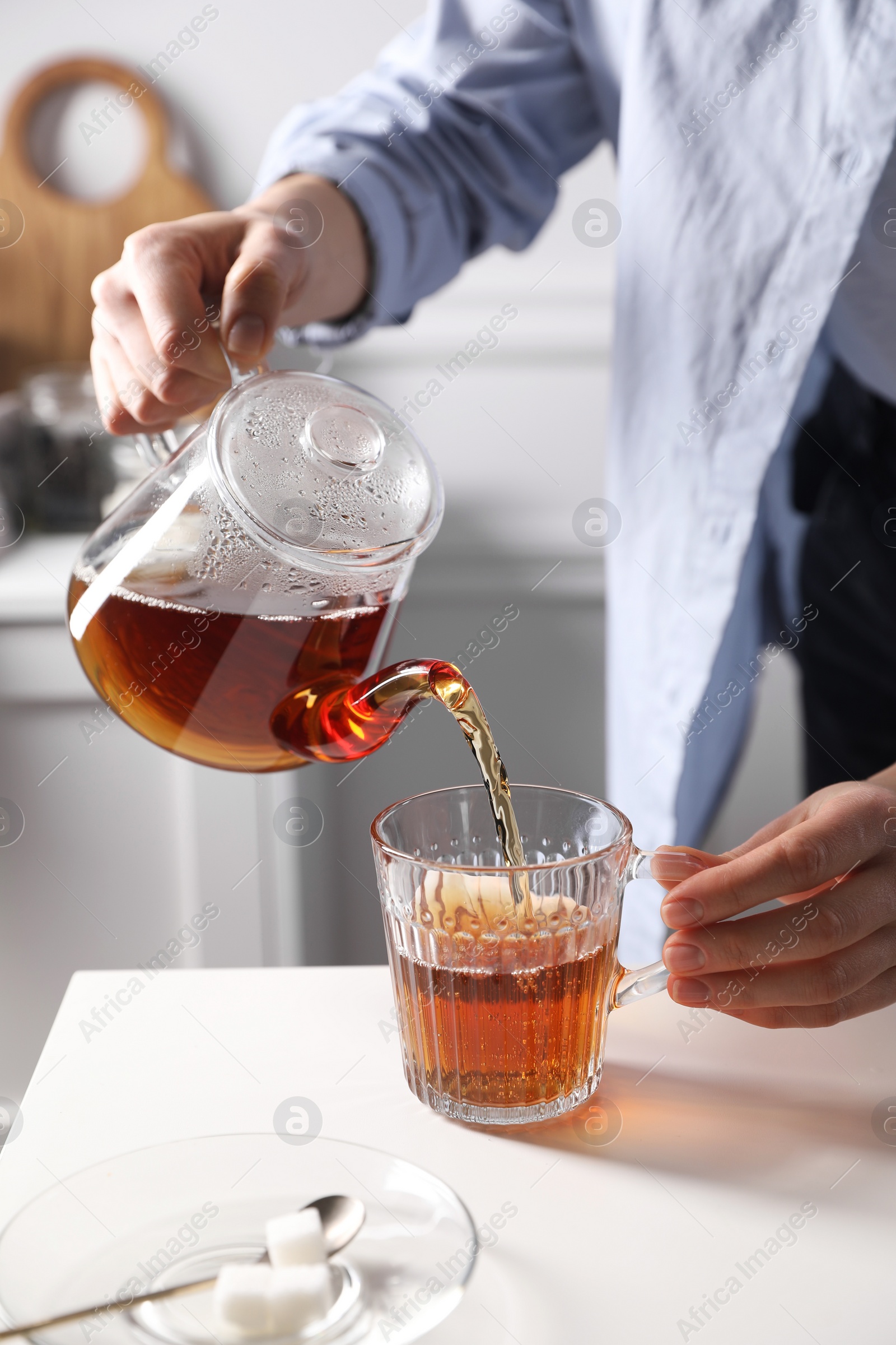 Photo of Woman pouring hot tea into cup at white table, closeup