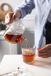 Woman pouring hot tea into cup at white table, closeup