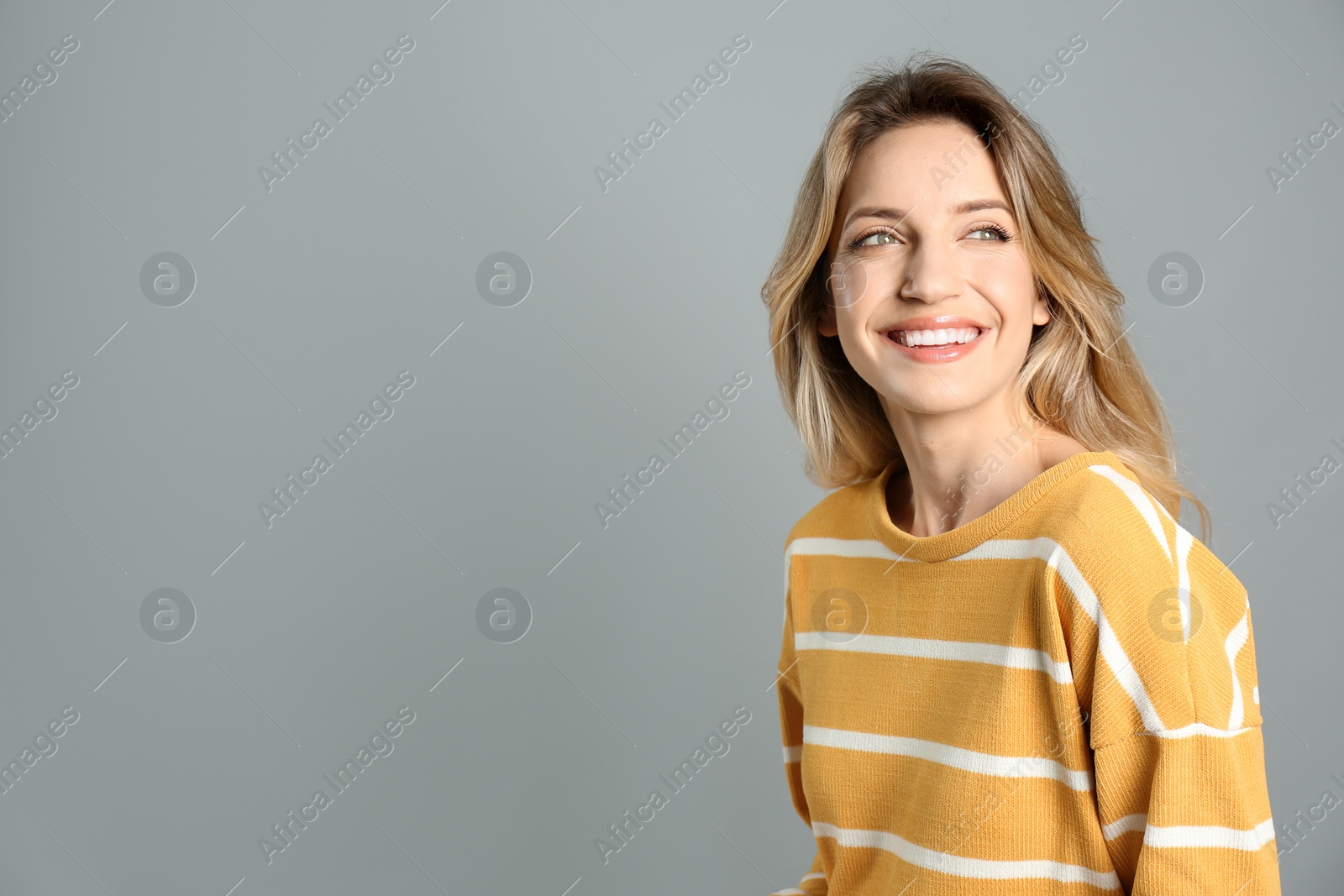 Photo of Portrait of happy young woman with beautiful blonde hair and charming smile on grey background. Space for text