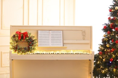 Photo of White piano with festive decor and music sheets near Christmas tree indoors