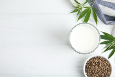 Photo of Glass of fresh hemp milk, seeds and leaves on white wooden table, flat lay. Space for text