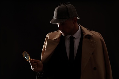 Photo of Old fashioned detective with magnifying glass on dark background