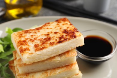 Delicious turnip cake with arugula and soy sauce on plate, closeup
