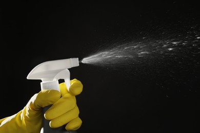 Photo of Woman spraying liquid from bottle on black background, closeup