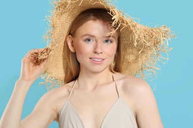 Beautiful young woman in straw hat on light blue background