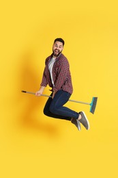 Young man with broom jumping on orange background