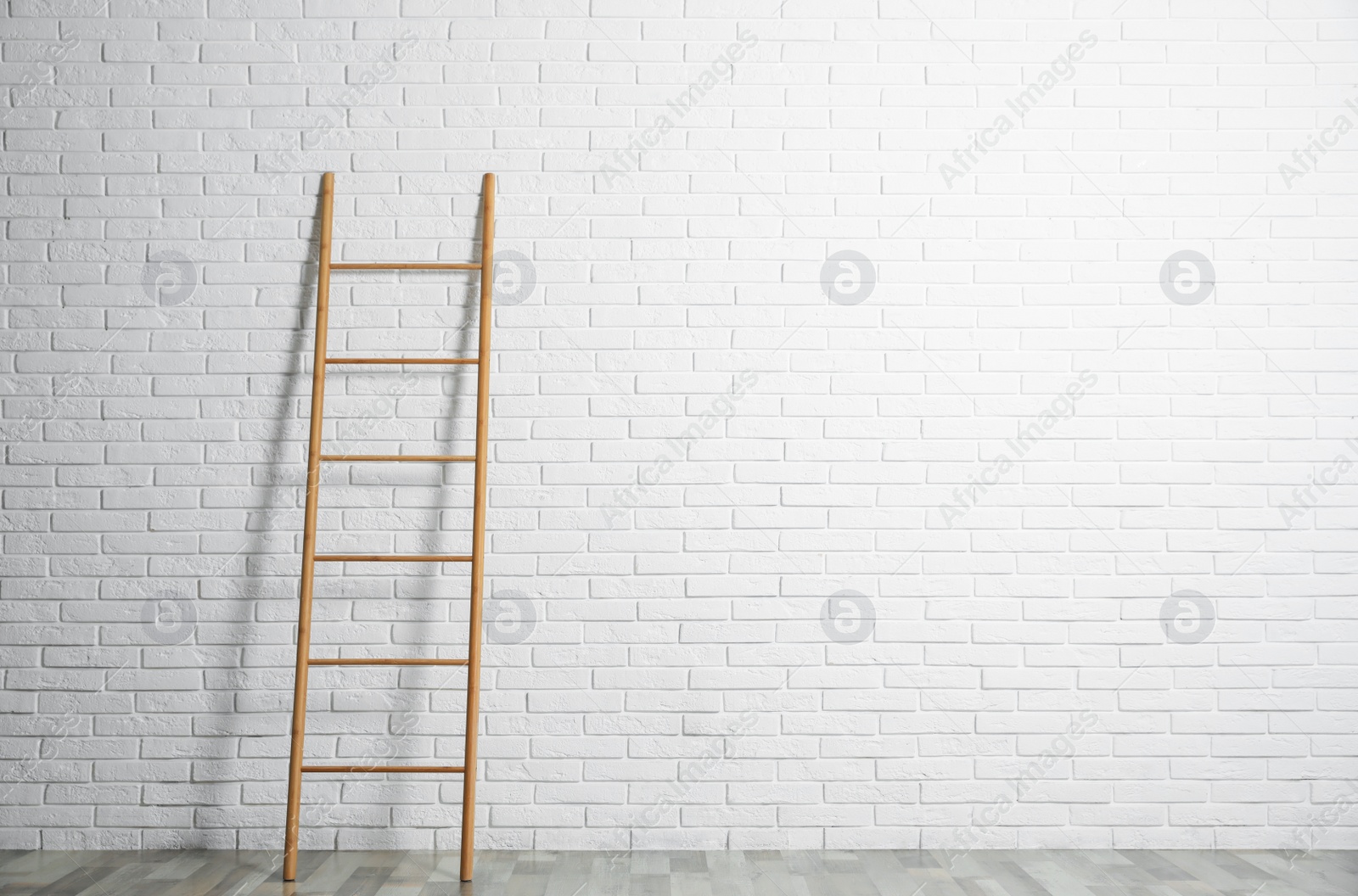 Photo of Modern wooden ladder near white brick wall. Space for text