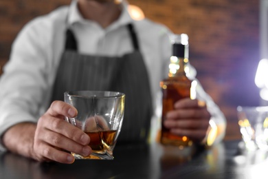 Photo of Bartender with glass and bottle of whiskey at counter in bar, closeup. Space for text