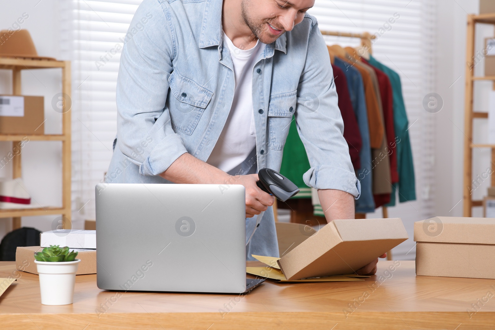 Photo of Seller with scanner reading parcel barcode at table in office, closeup. Online store