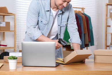 Photo of Seller with scanner reading parcel barcode at table in office, closeup. Online store