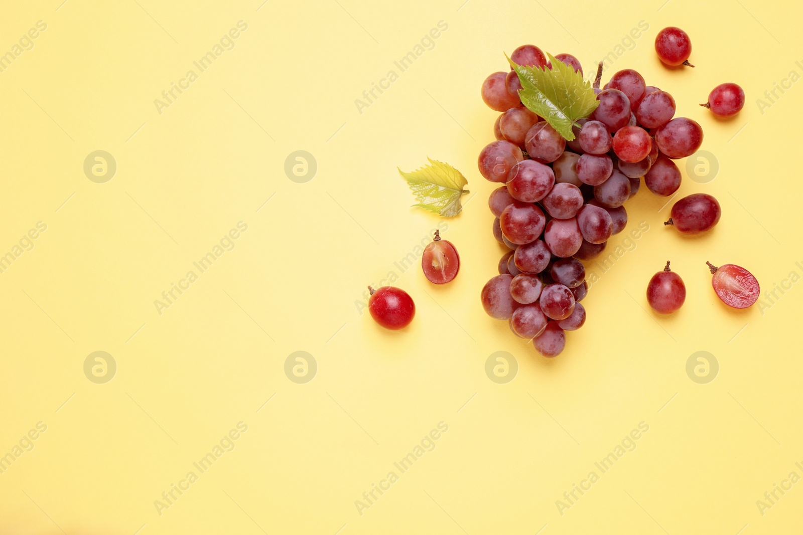 Photo of Bunch of ripe red grapes with green leaves on yellow background, flat lay. Space for text