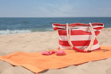 Photo of Soft orange beach towel, bag and flip flops on sandy seashore, space for text