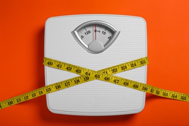 Scales and measuring tape on orange background, top view. Weight loss concept