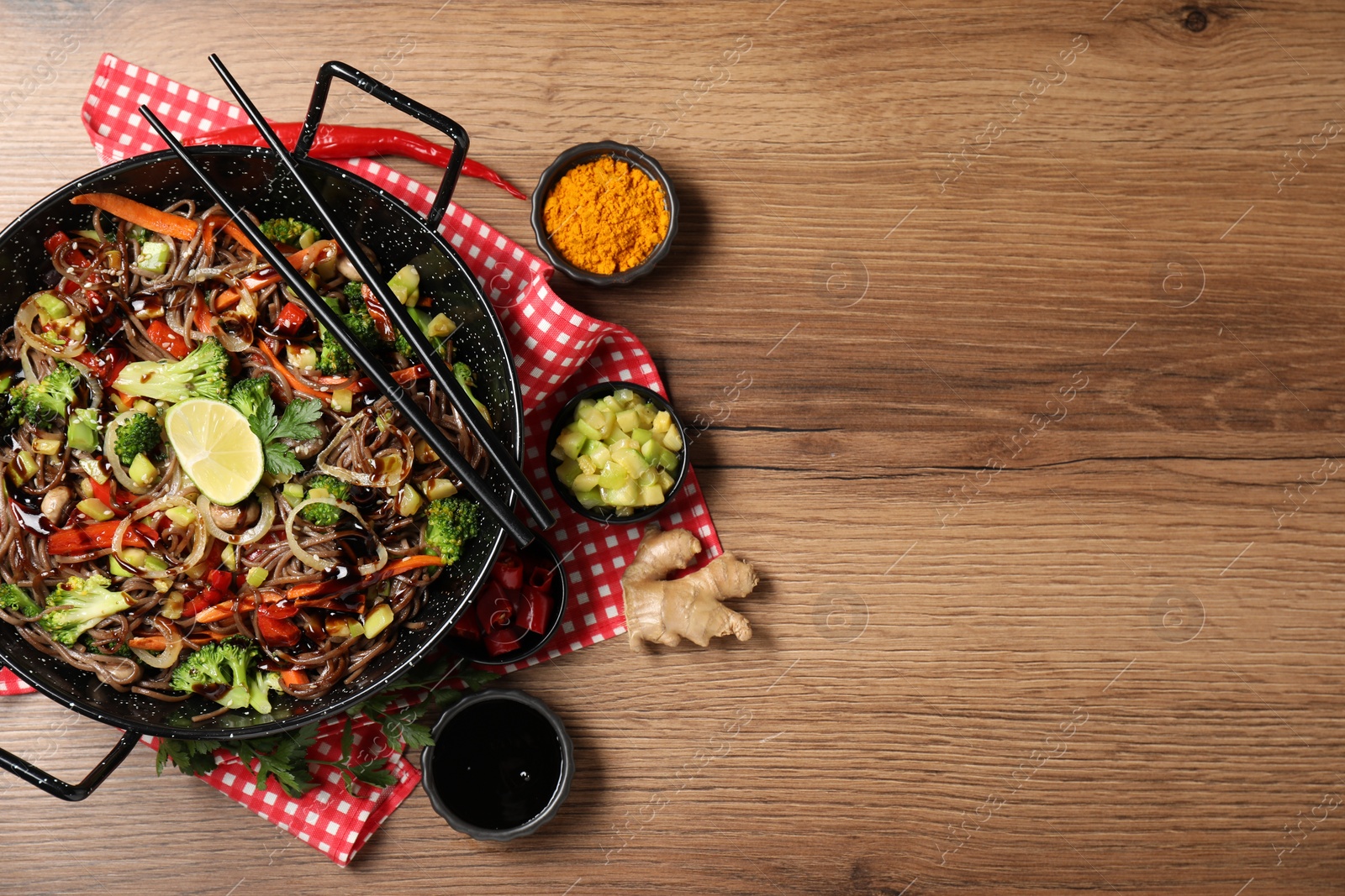 Photo of Stir-fry. Tasty noodles with meat in wok, chopsticks and ingredients on wooden table, flat lay. Space for text