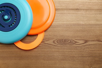Plastic frisbee disks and ring on wooden background, flat lay. Space for text