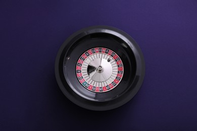 Photo of Roulette wheel with ball on dark violet background, top view. Casino game