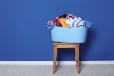 Photo of Laundry basket with dirty clothes on stool near color wall
