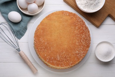 Plate with delicious sponge cake and ingredients on white wooden table, flat lay