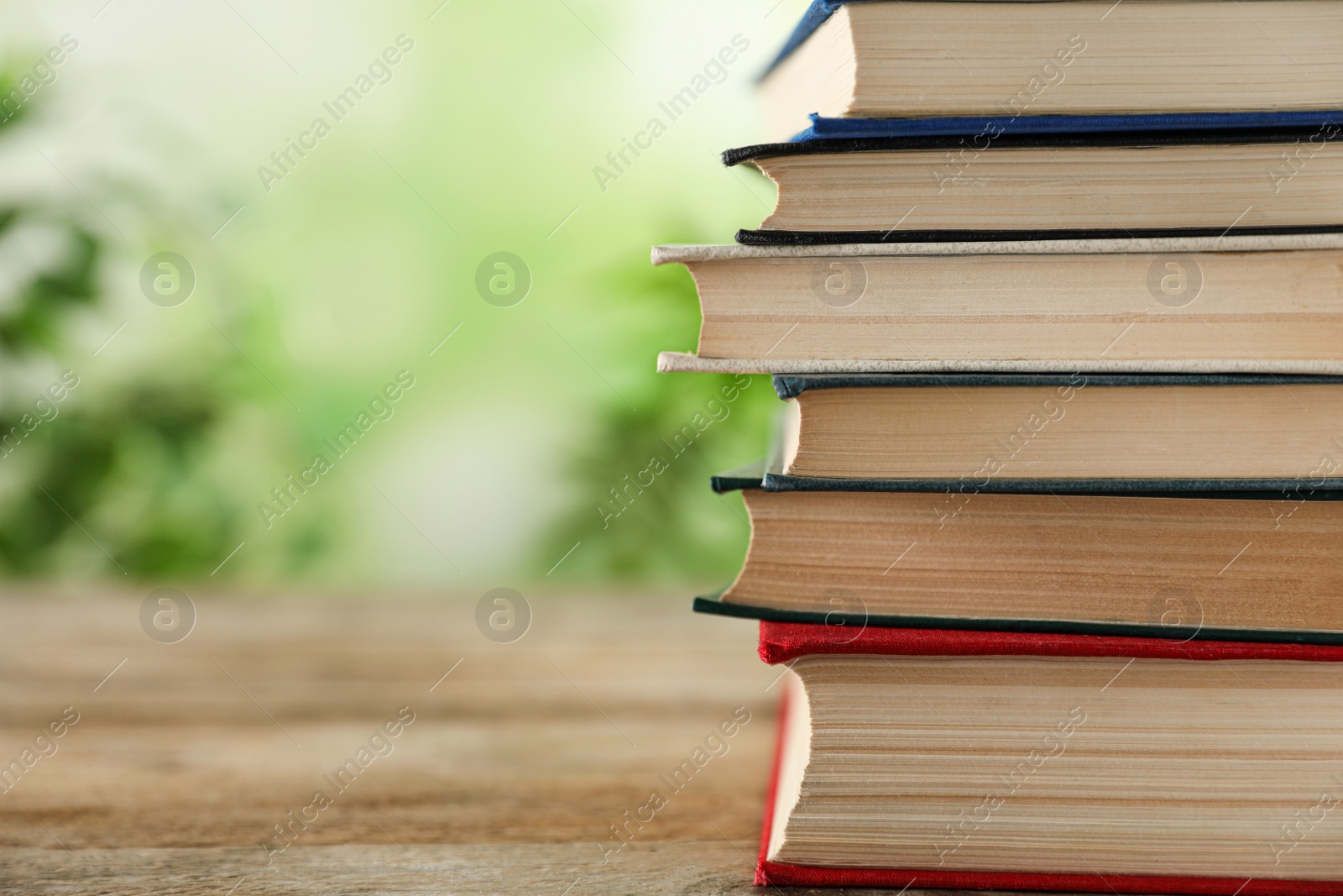 Photo of Stack of hardcover books on wooden table against blurred background. Space for text