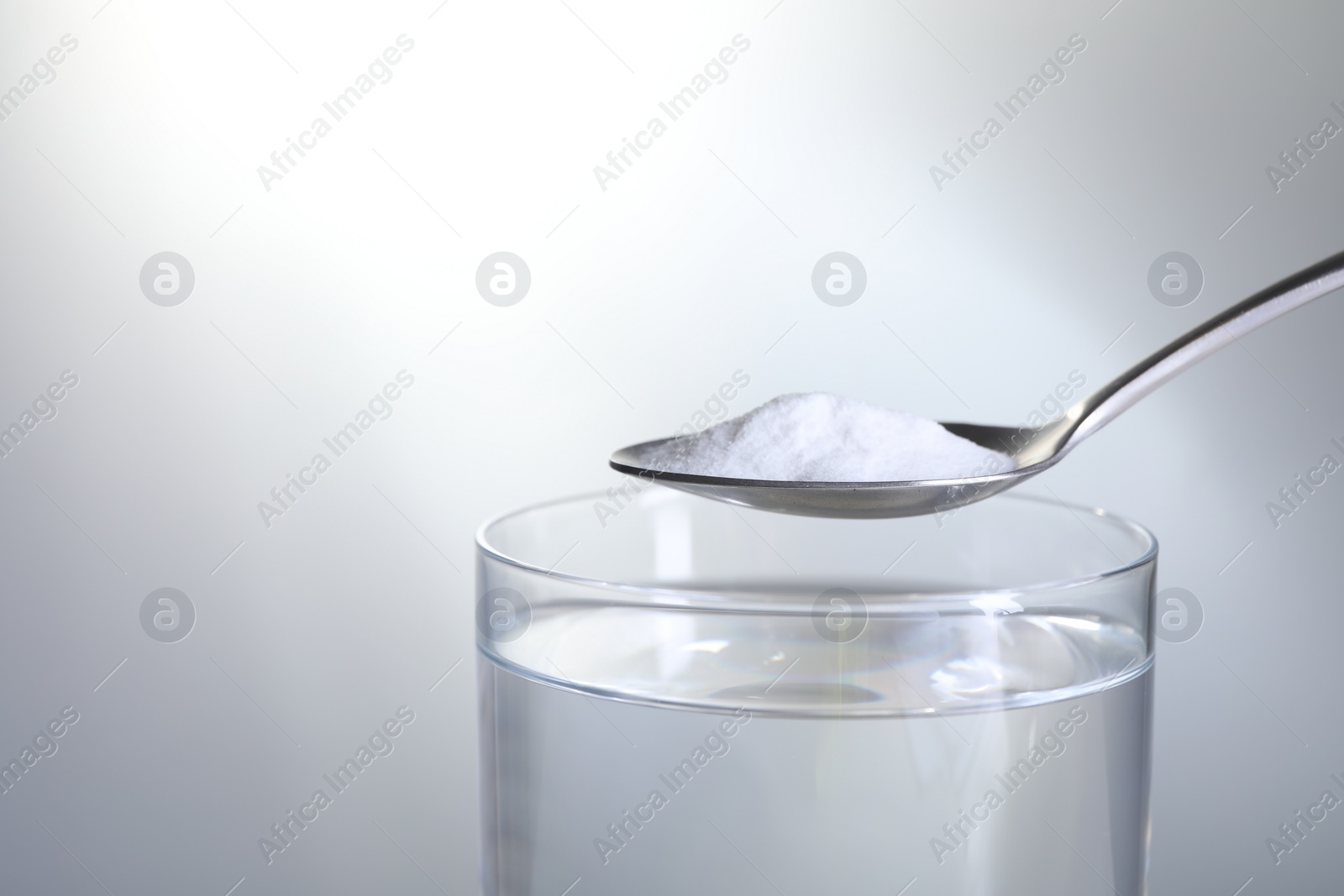 Photo of Spoon with baking soda over glass of water on light grey background, closeup. Space for text