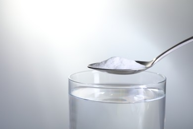 Photo of Spoon with baking soda over glass of water on light grey background, closeup. Space for text