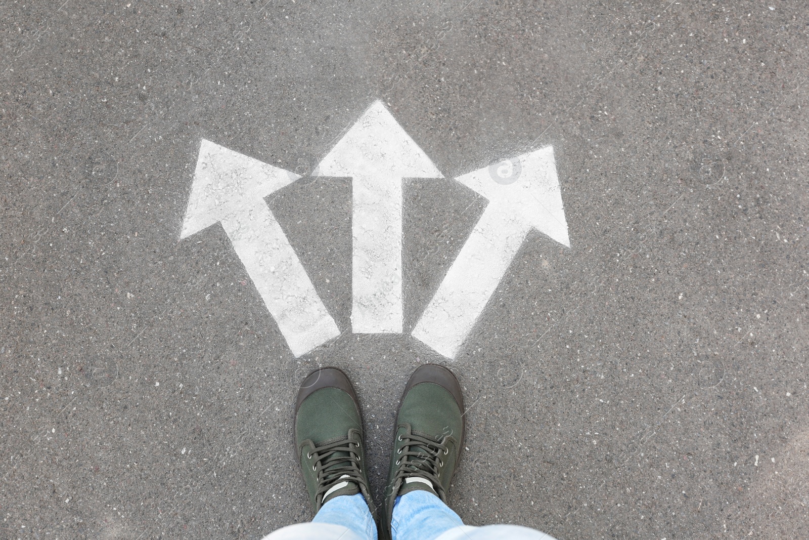 Photo of Woman standing near arrows on asphalt, top view. Choice concept