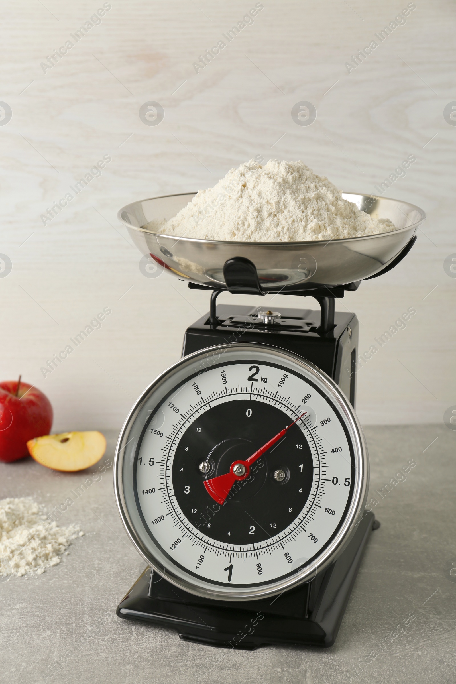 Photo of Kitchen scale with flour and ripe apples on grey table