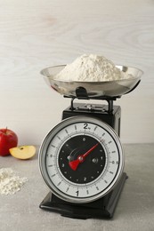 Kitchen scale with flour and ripe apples on grey table