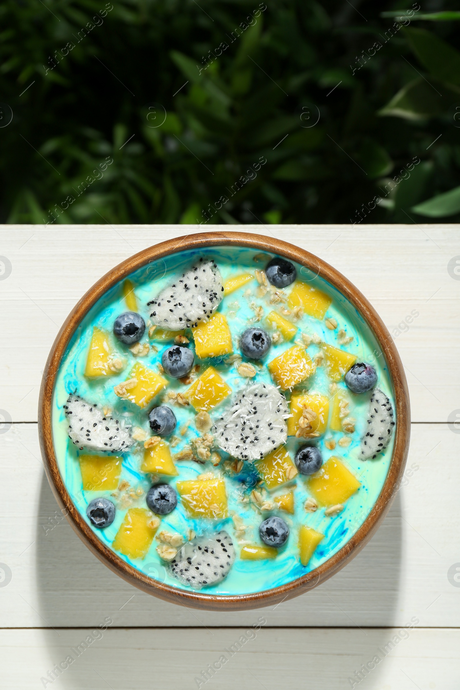 Photo of Delicious smoothie bowl with fresh fruits, blueberries and oatmeal on white wooden table outdoors, top view