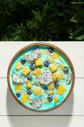 Delicious smoothie bowl with fresh fruits, blueberries and oatmeal on white wooden table outdoors, top view