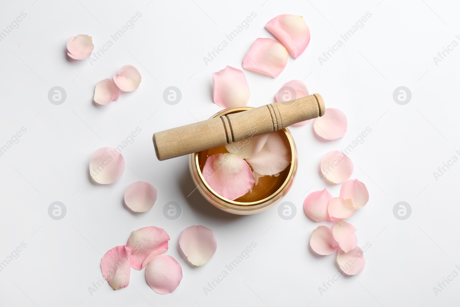 Photo of Golden singing bowl with petals and mallet on white background, flat lay. Sound healing